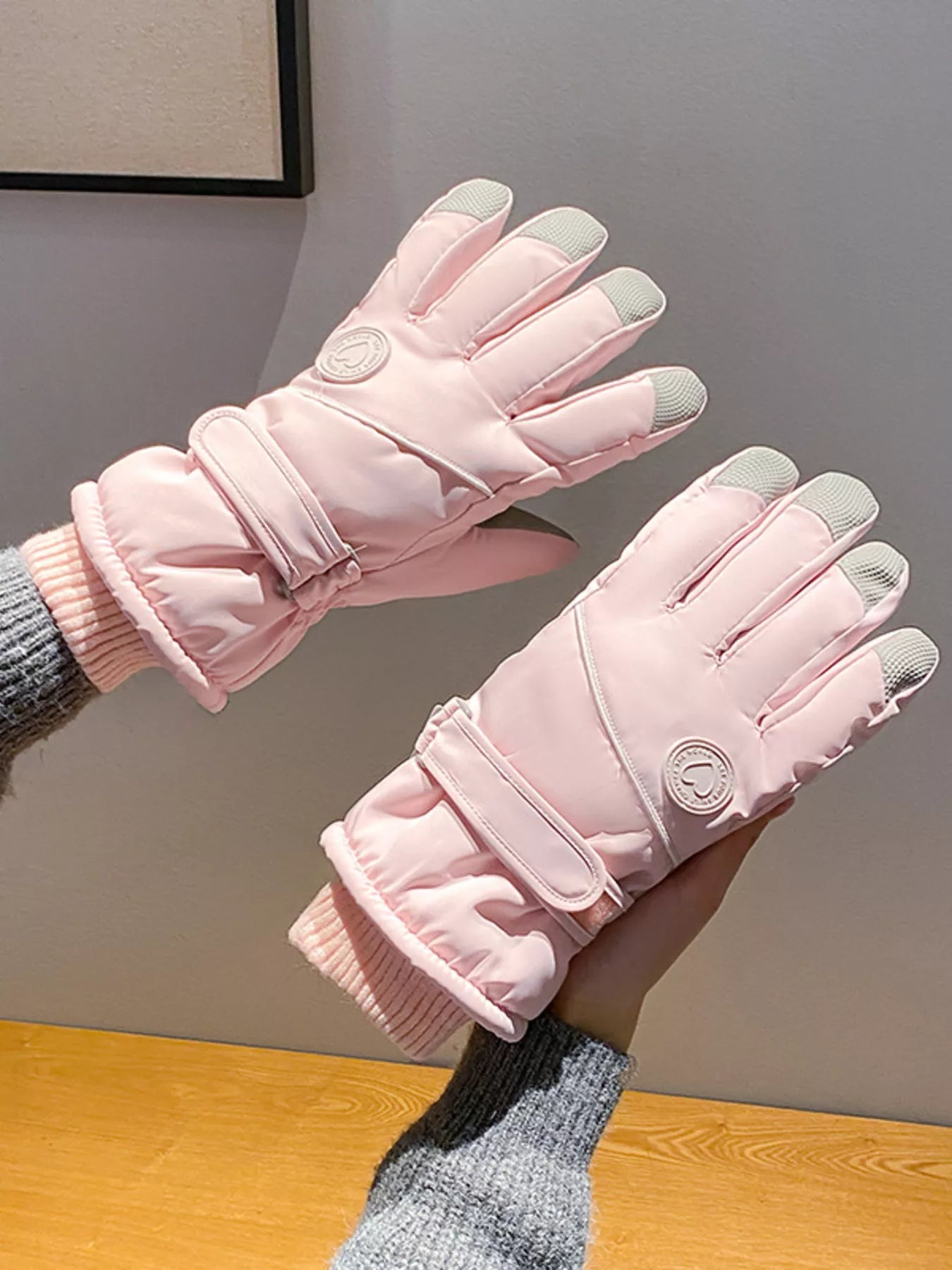 Pink gloves with gray accents held in hands against a neutral background