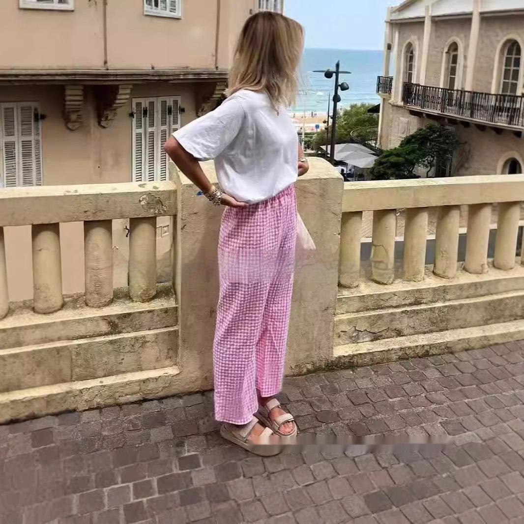 Woman in white shirt and pink pants standing on a balcony with ocean view