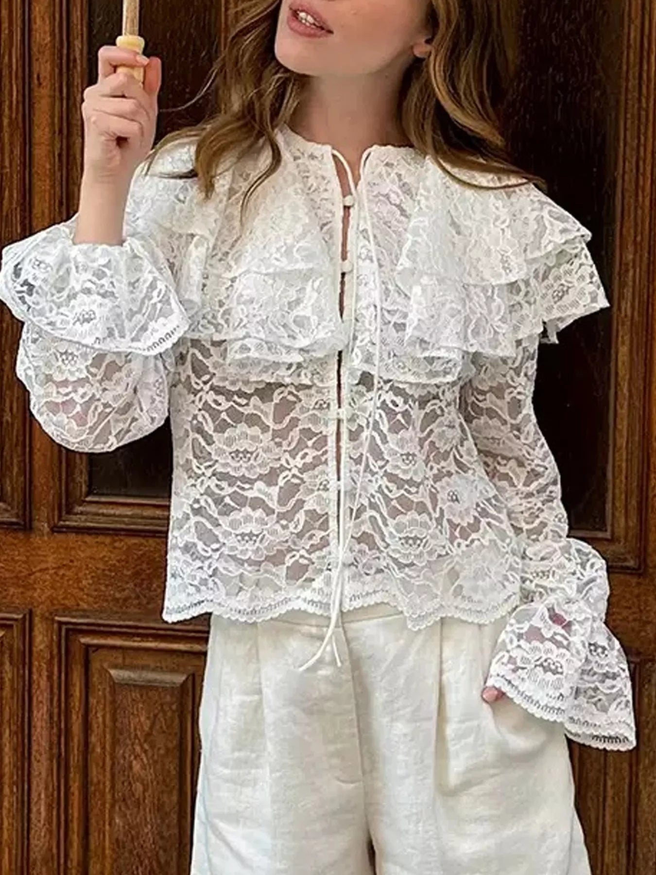 Person wearing a white lace blouse with ruffled sleeves against a wooden background