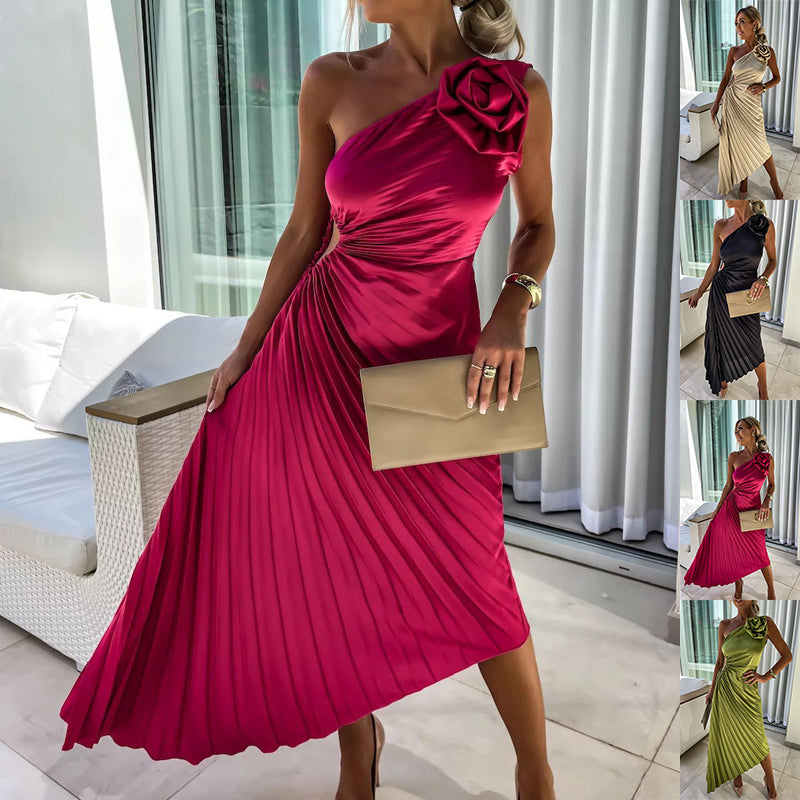 Woman in a pink one-shoulder dress with a large flower detail, holding a beige clutch, in an indoor setting.
