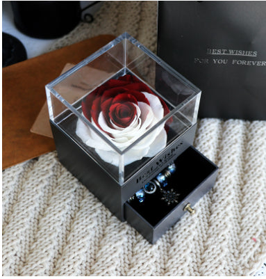 Glass box with a preserved rose and jewelry on a textured surface