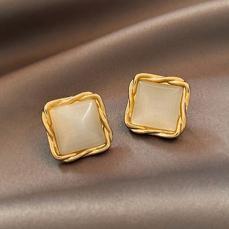 Gold square earrings with beige stones on a brown fabric background