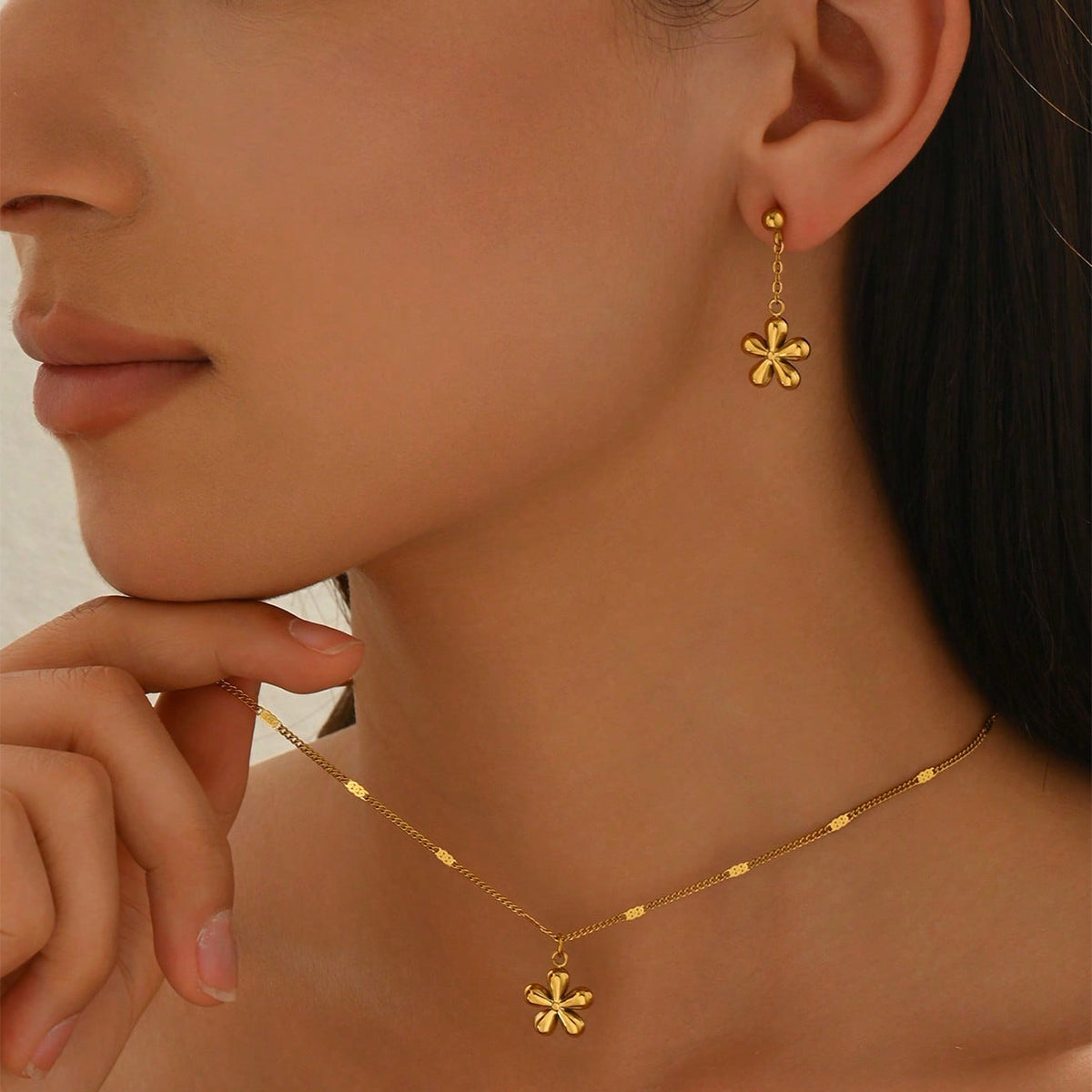 Close-up of a person wearing gold earrings and necklace with a neutral background