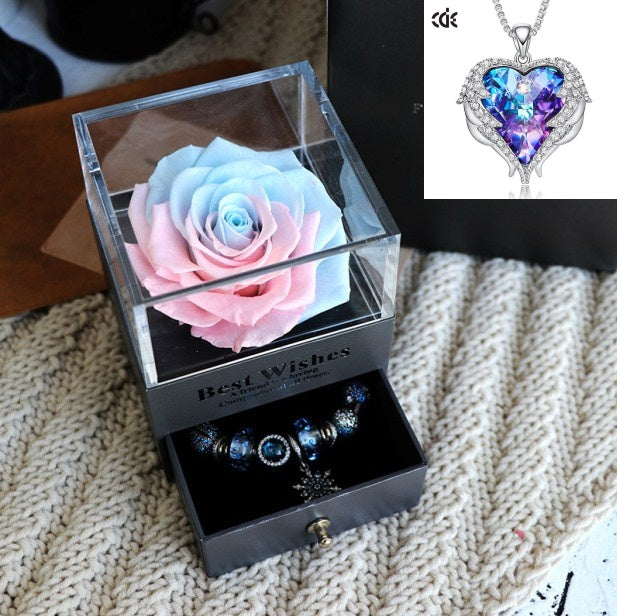Clear box with a rose and jewelry set on a textured surface, with a heart-shaped pendant in the corner.