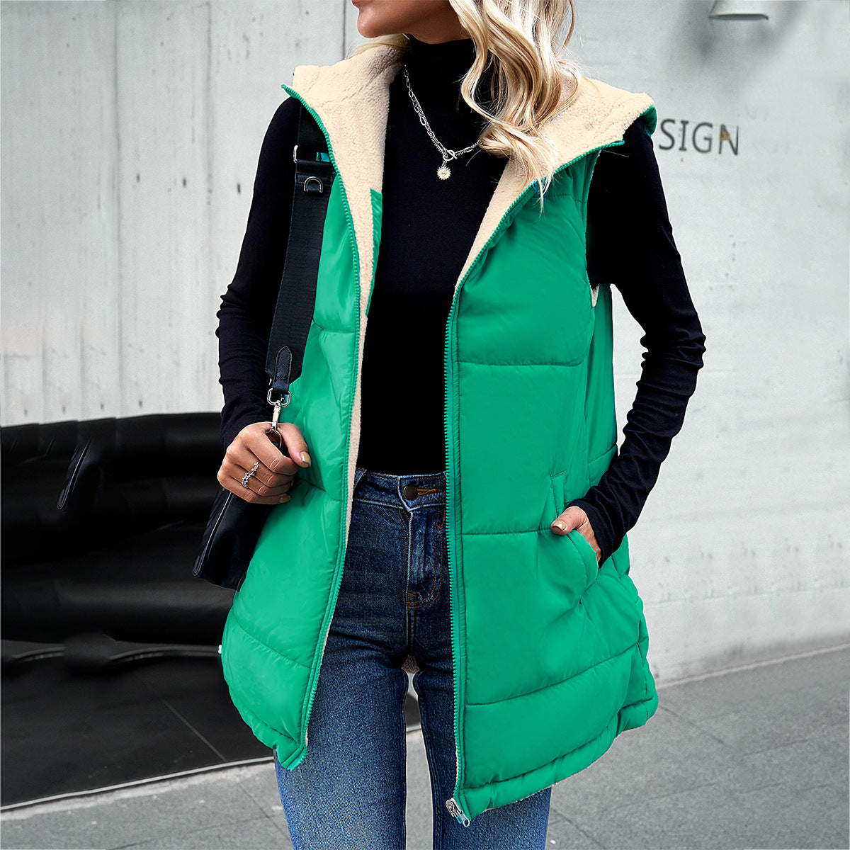 Person wearing a green puffer vest with beige lining in an urban setting.