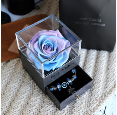 Glass box with a preserved rose and jewelry on a textured surface