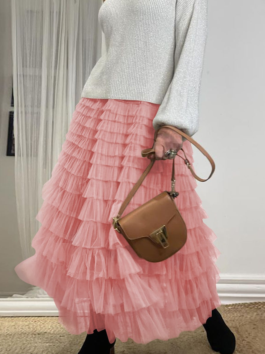 Person wearing a pink ruffled skirt and holding a brown handbag indoors.