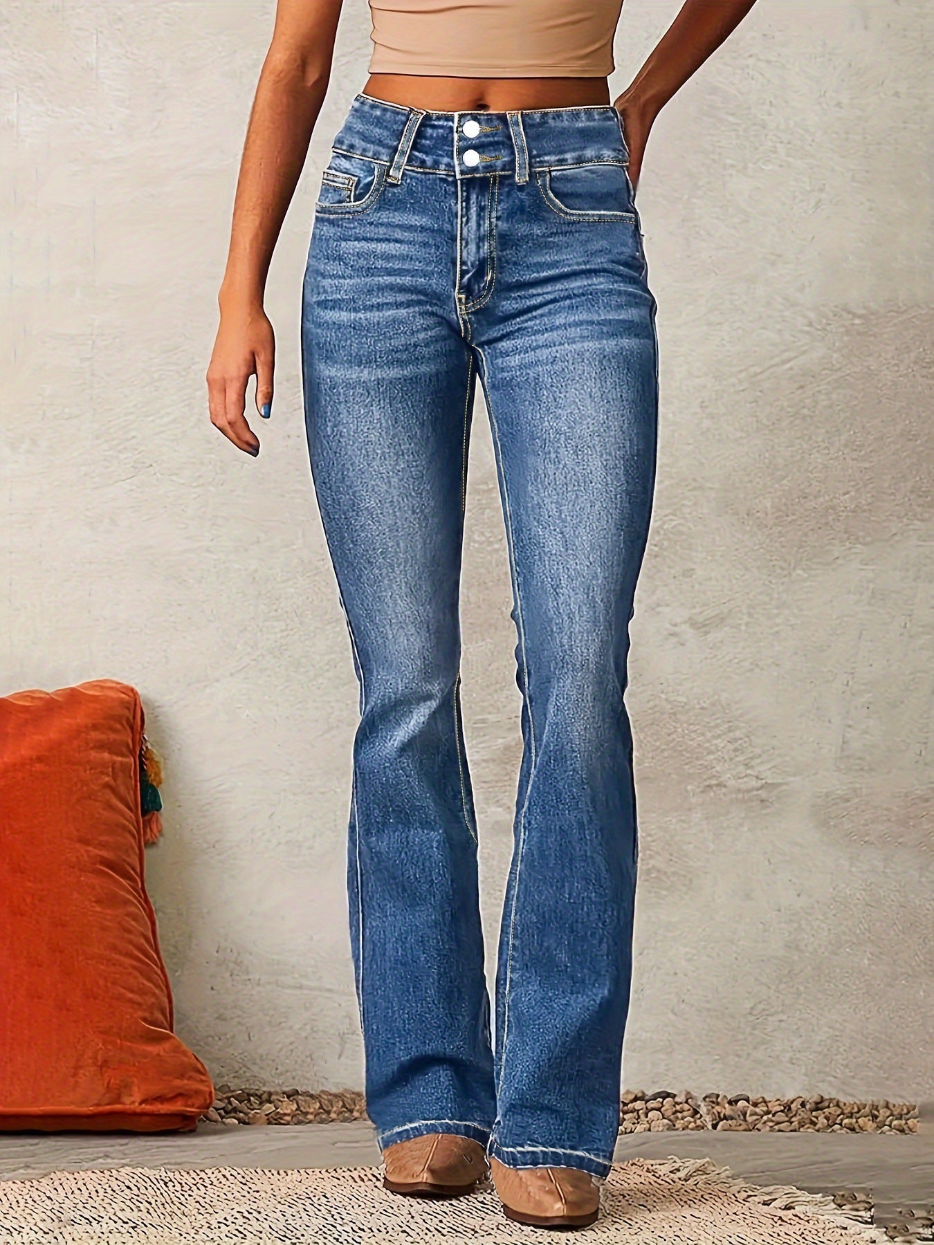 Person wearing blue jeans standing against a neutral wall with an orange pillow on the floor.