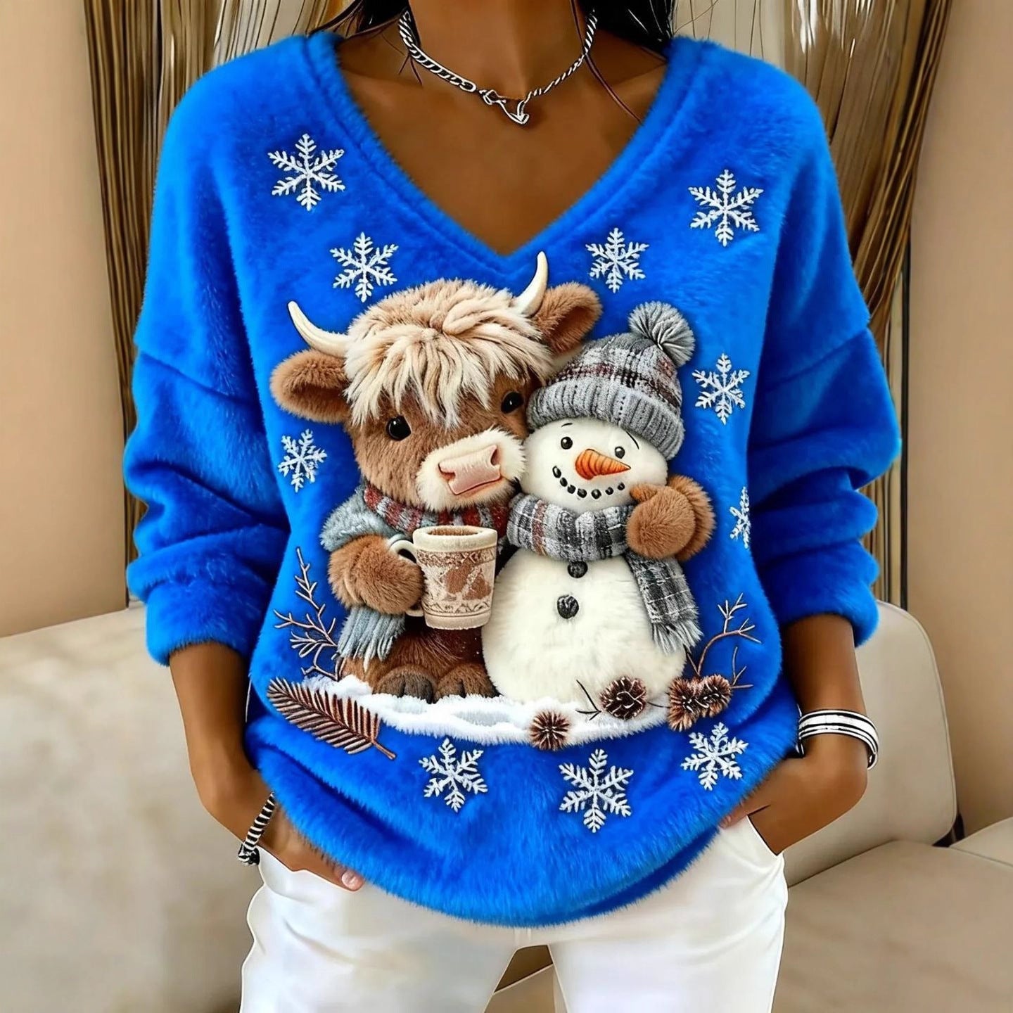 Blue sweater with a cow and snowman design on a neutral background
