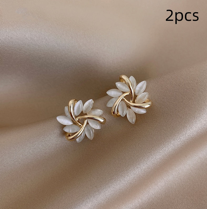 Pair of gold and white leaf-shaped earrings on a beige fabric background