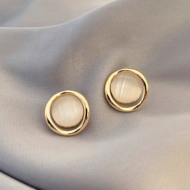 Gold earrings with round white stones on a light fabric background