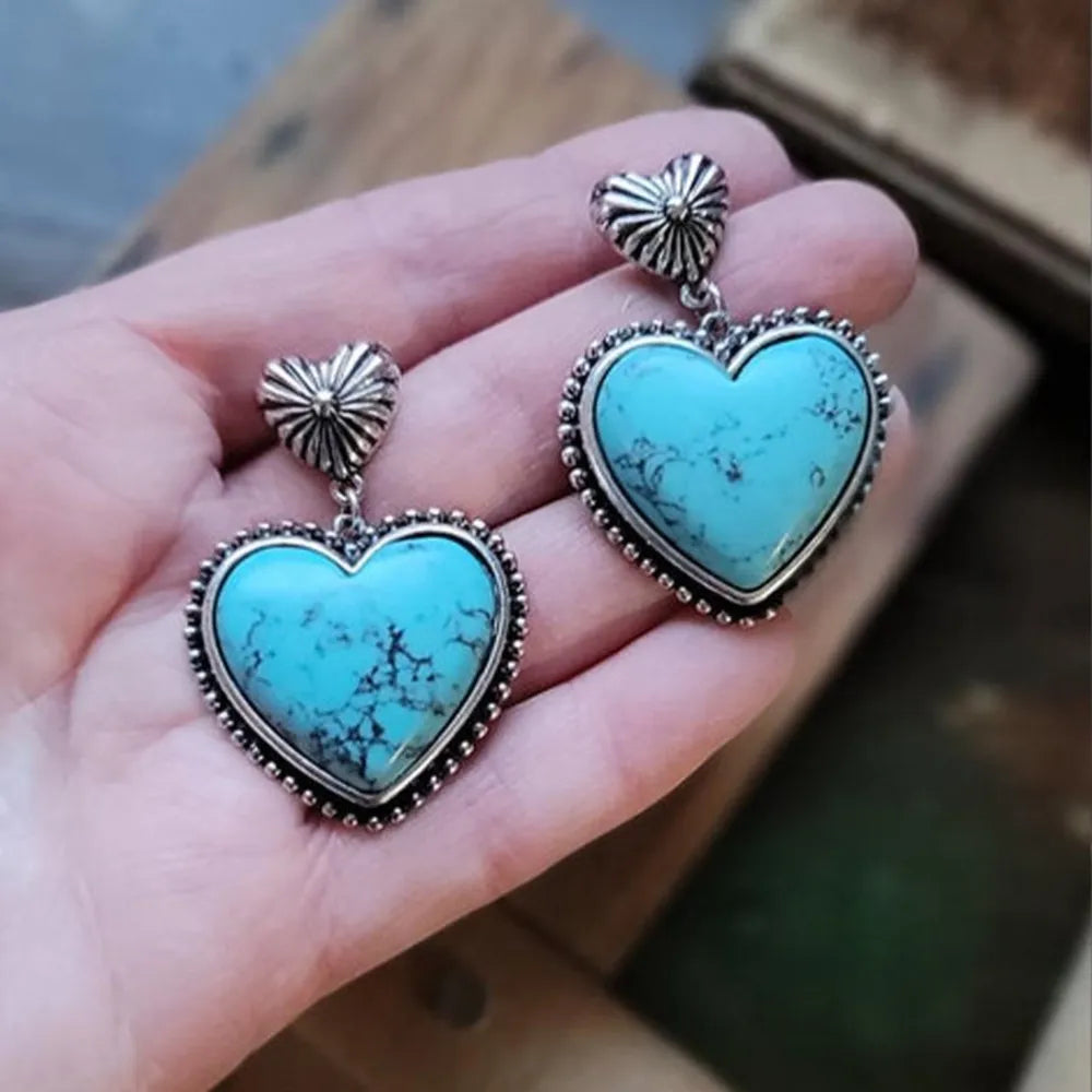 Heart-shaped turquoise earrings with silver accents held in a hand.