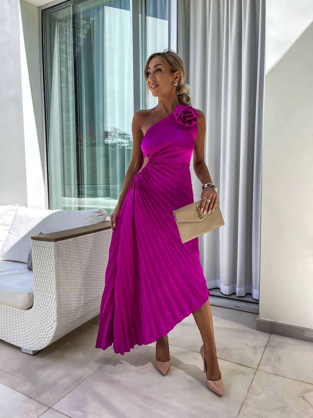 Woman in a vibrant pink dress with a floral detail, standing in a modern room.