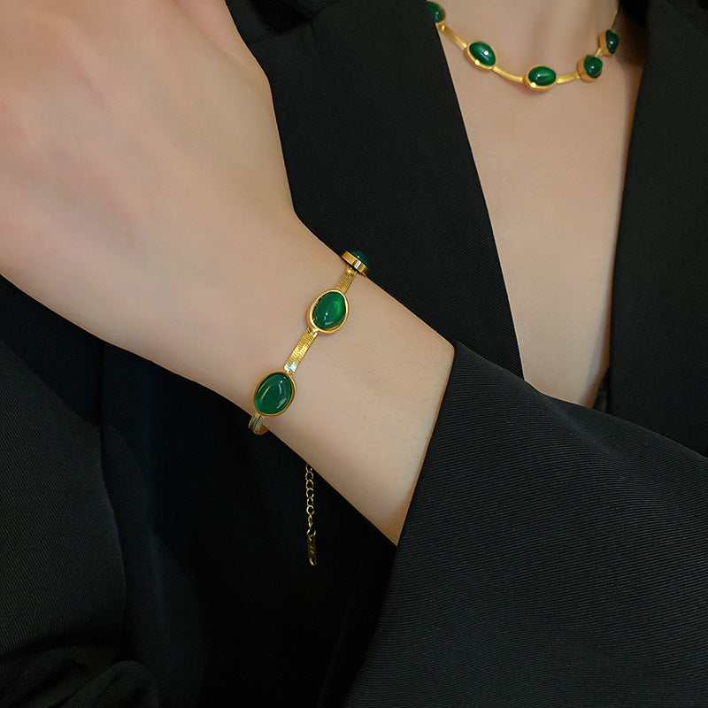 Gold bracelet with green stones on a wrist, wearing a black outfit.