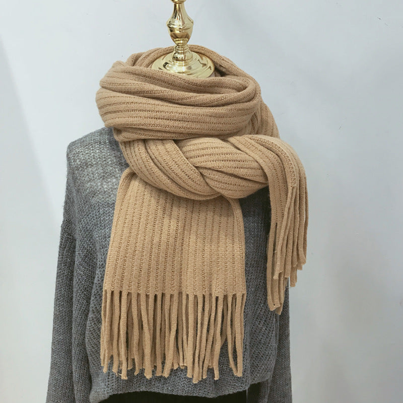 Beige scarf with fringe draped over a gray sweater on a mannequin against a white background