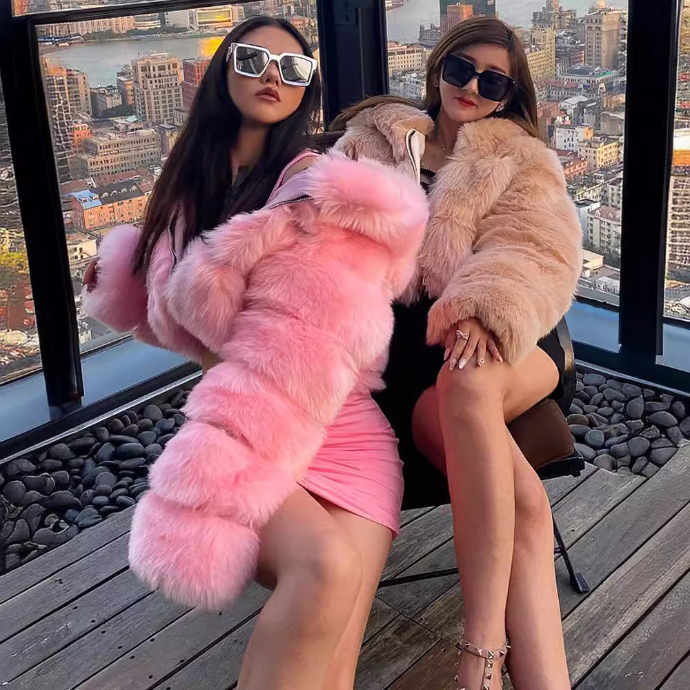Two women in fur coats sitting on a rooftop with a cityscape view.