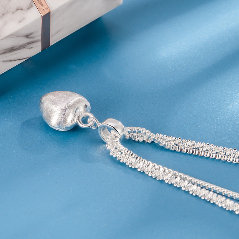 Silver necklace with a heart-shaped pendant on a blue surface