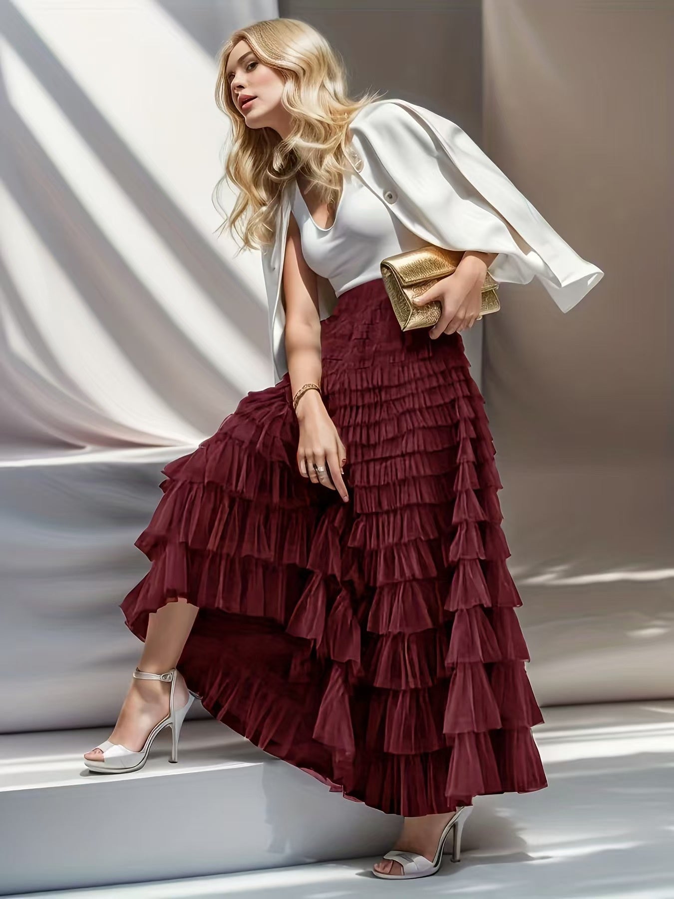 Woman wearing a white top and burgundy ruffled skirt with a gold clutch.