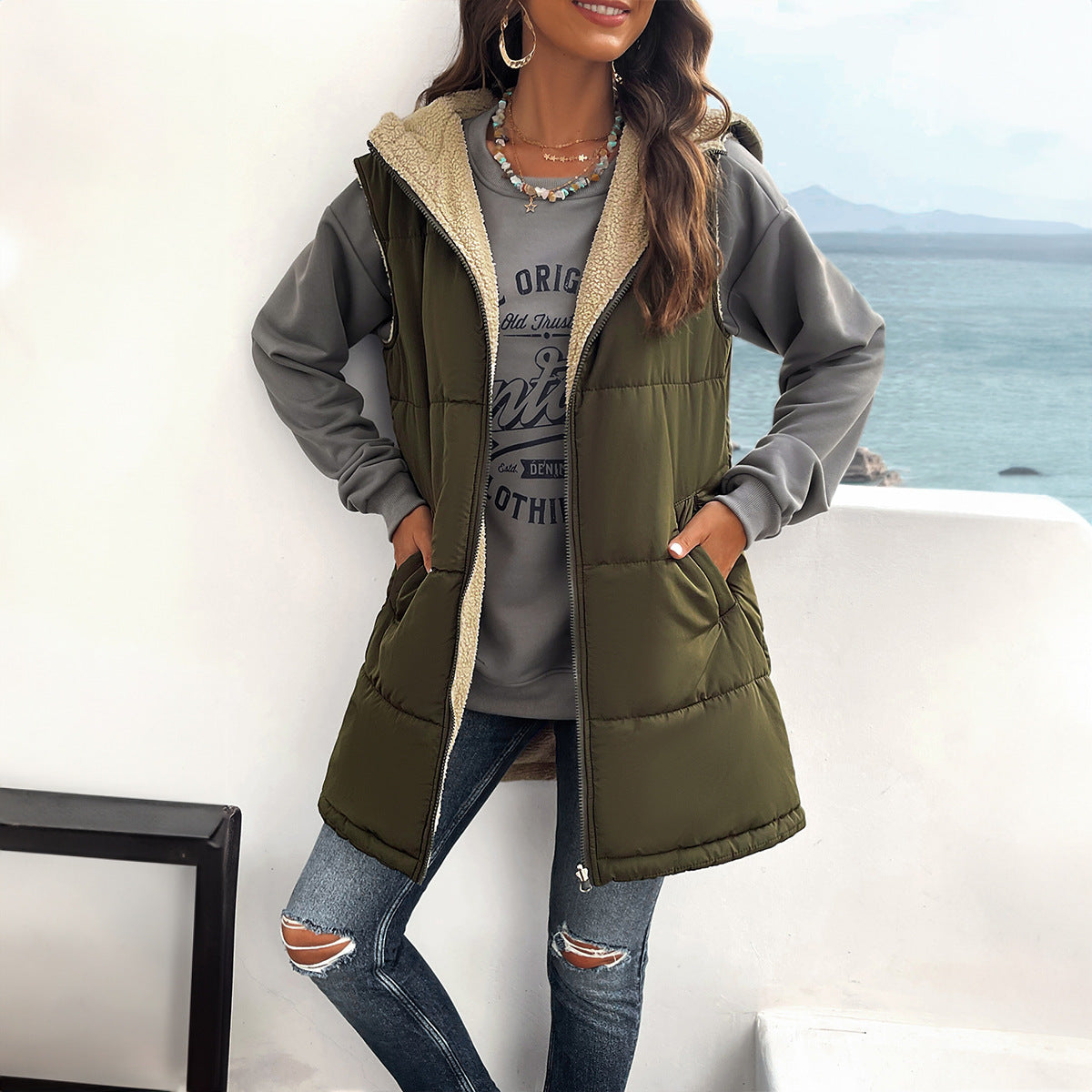 Woman wearing a green puffer vest with a blurred coastal background