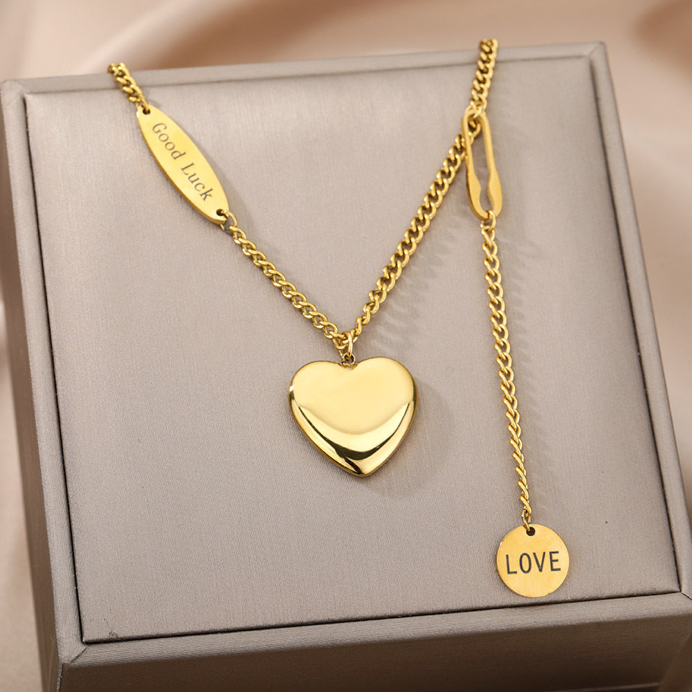 Gold heart-shaped pendant necklace with 'Good Luck' and 'Love' tags on a gray box.
