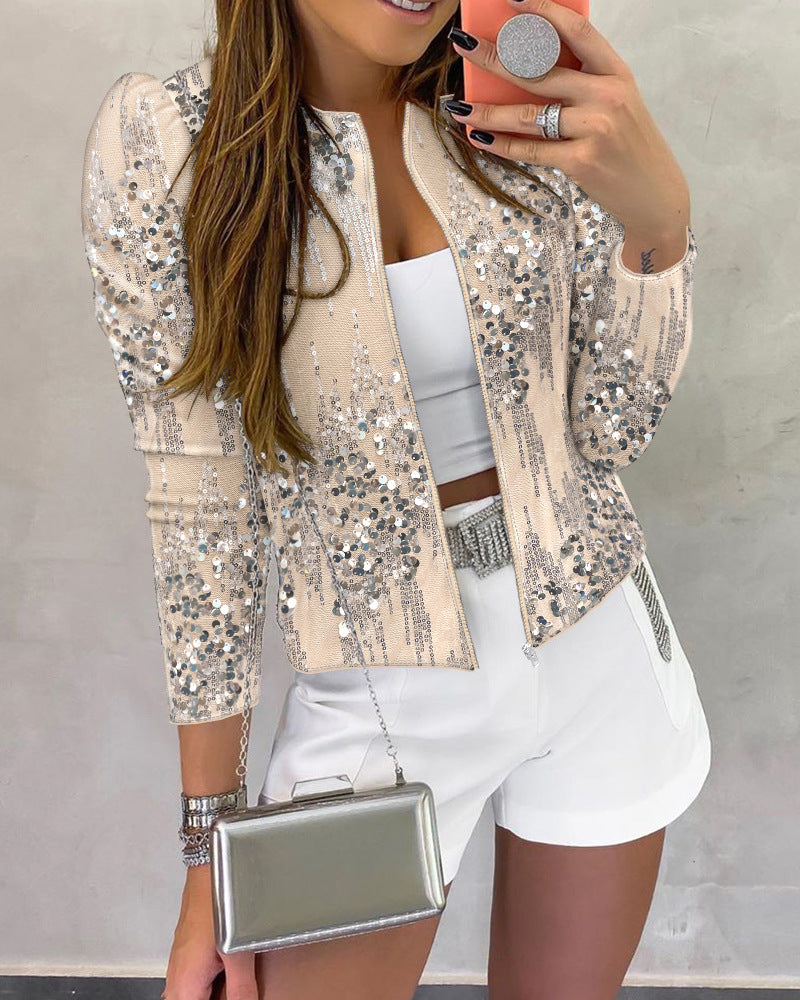 Woman wearing a sequin jacket and white shorts, holding a phone and clutch.