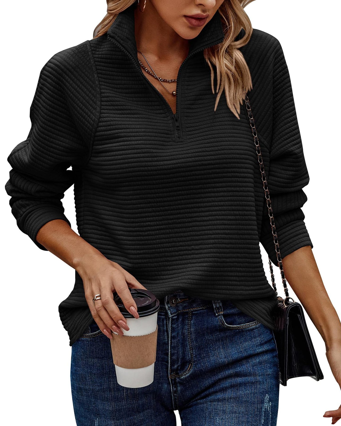 Woman wearing a black ribbed sweater and blue jeans, holding a coffee cup.