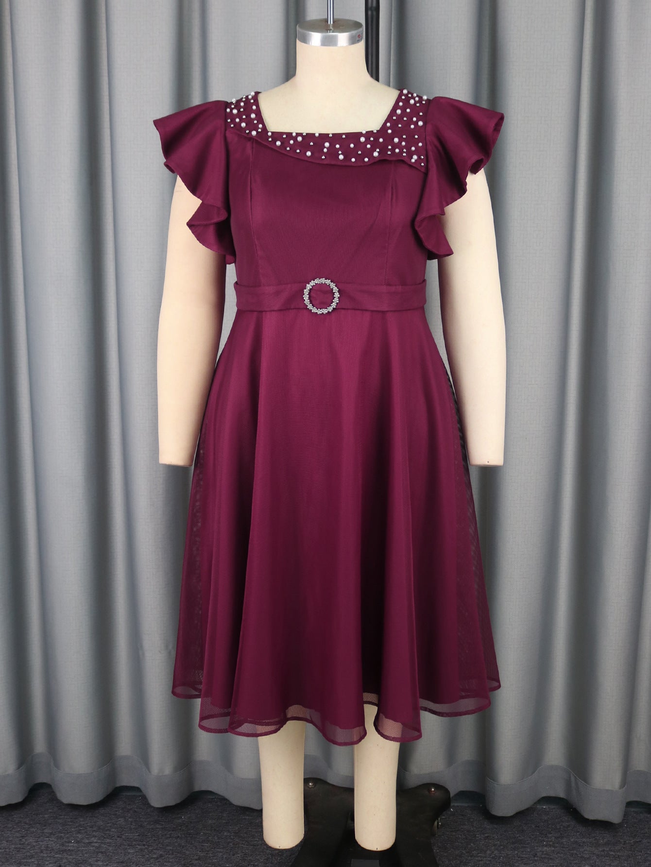 Maroon dress with ruffled sleeves on a mannequin against a gray curtain background