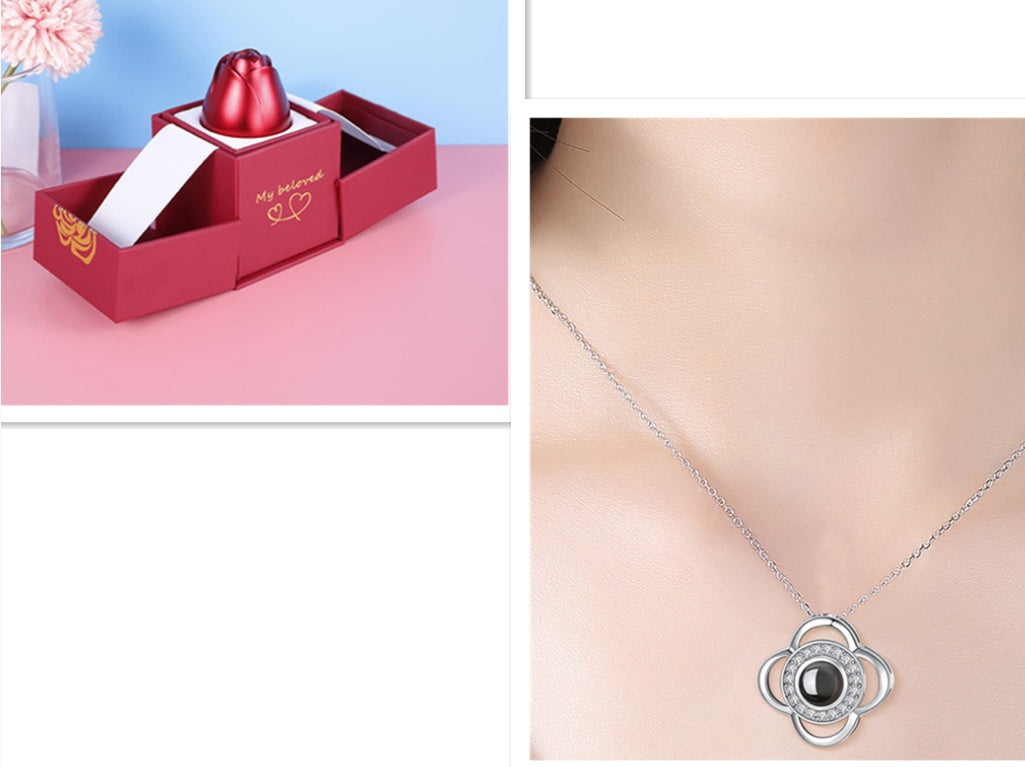 Red jewelry box with a heart design on a pink surface, next to a silver necklace with a black pendant.