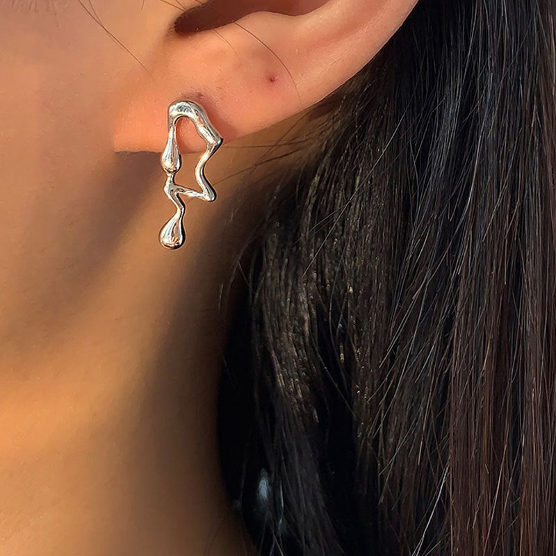 Silver earring worn on an ear with a blurred background