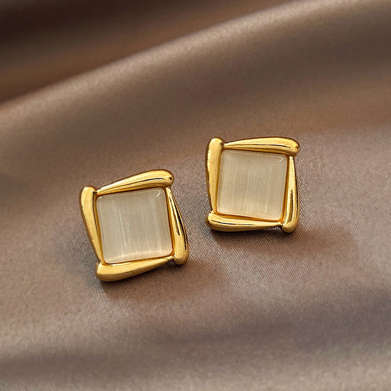 Gold square earrings with beige stones on a brown fabric background