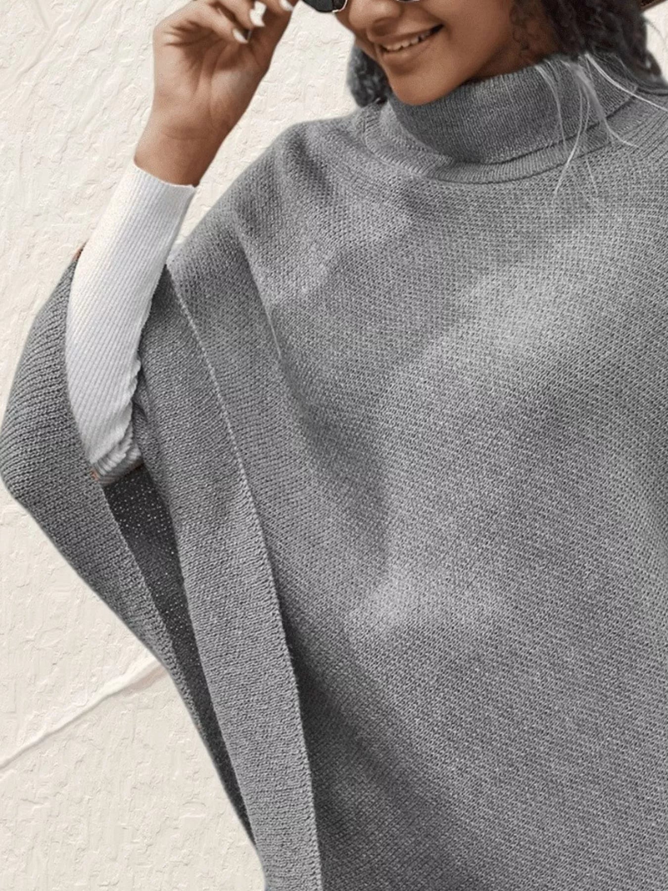 Person wearing a gray poncho over a light blue sweater on a neutral background