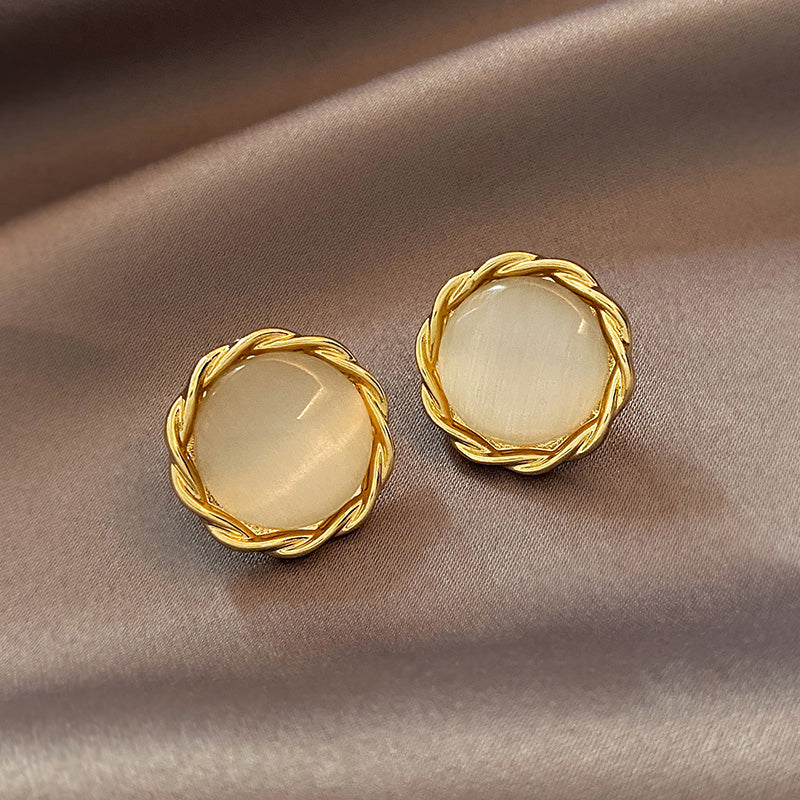 Pair of gold earrings with round beige stones on a brown fabric background