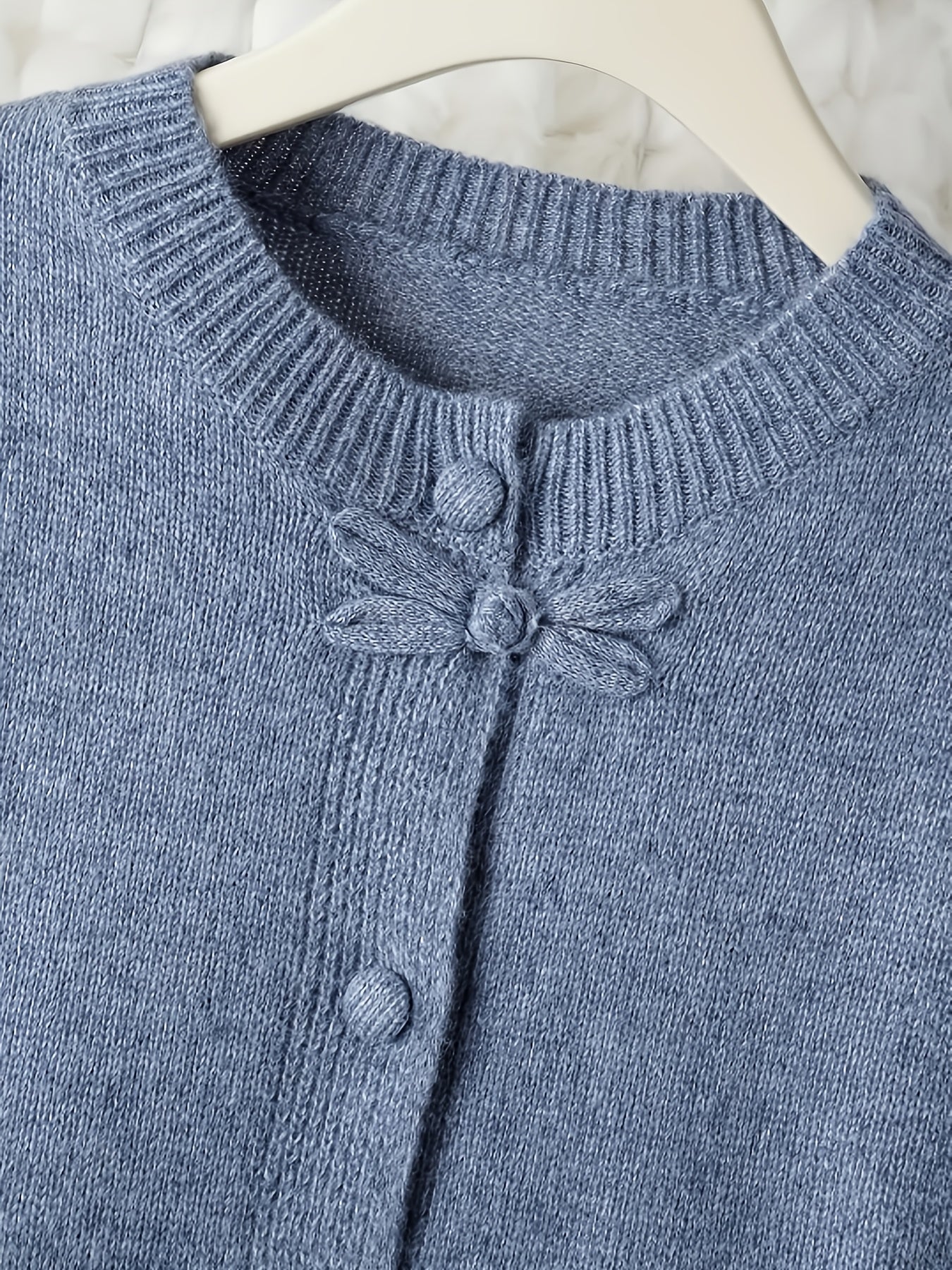 Blue knitted cardigan with button details on a white background