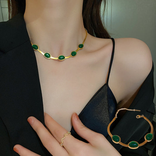 Woman wearing a gold necklace with green stones, holding a matching bracelet and ring.