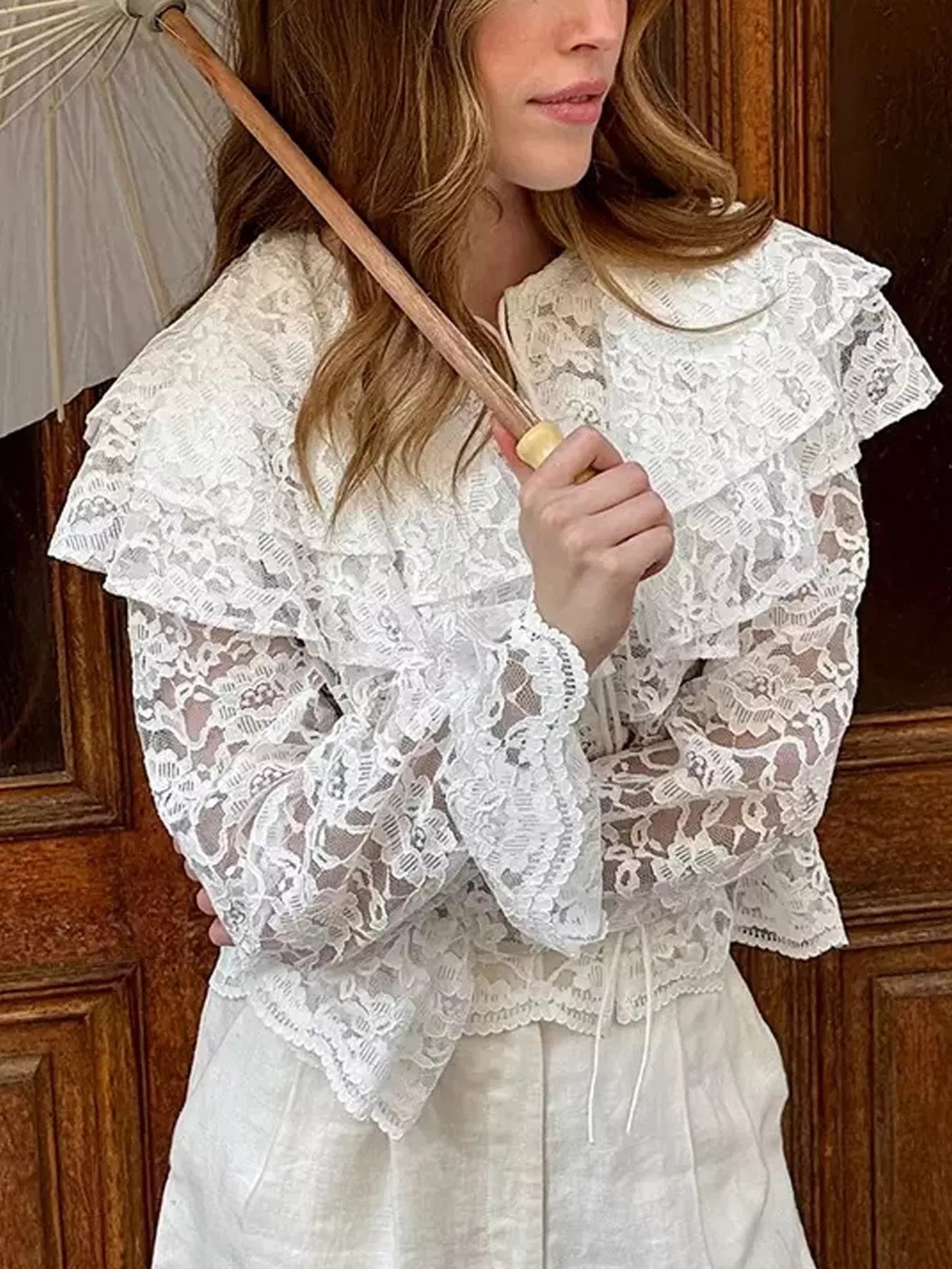 Woman wearing a white lace blouse holding an umbrella indoors.