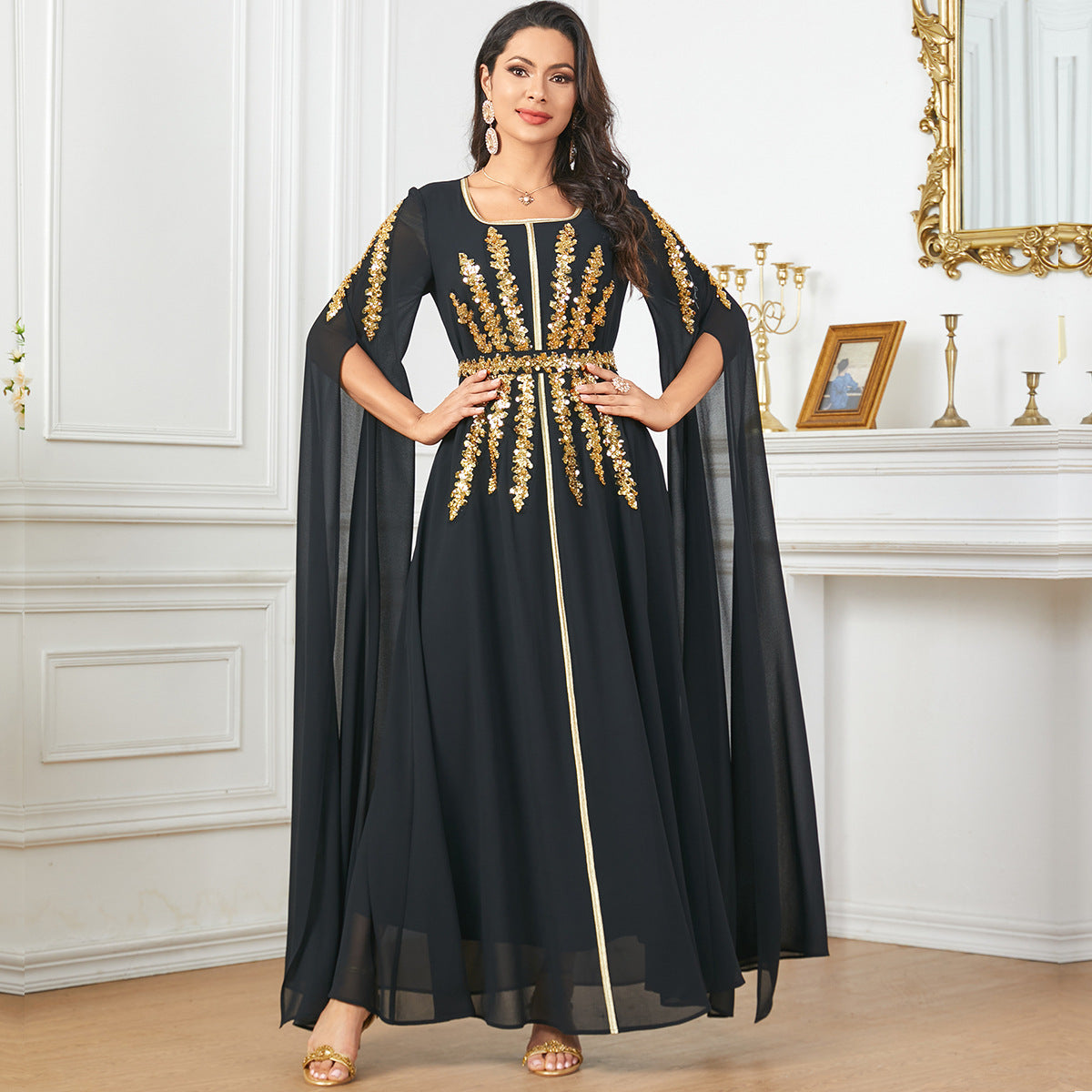 Woman wearing a black dress with gold embroidery in an elegant room.