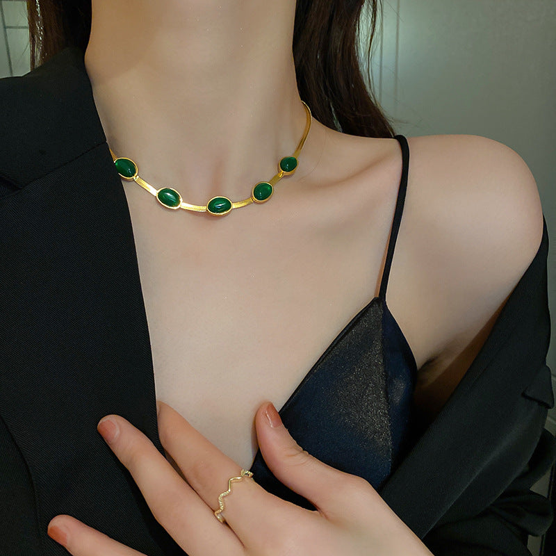 Gold necklace with green stones worn by a person, held by another hand.