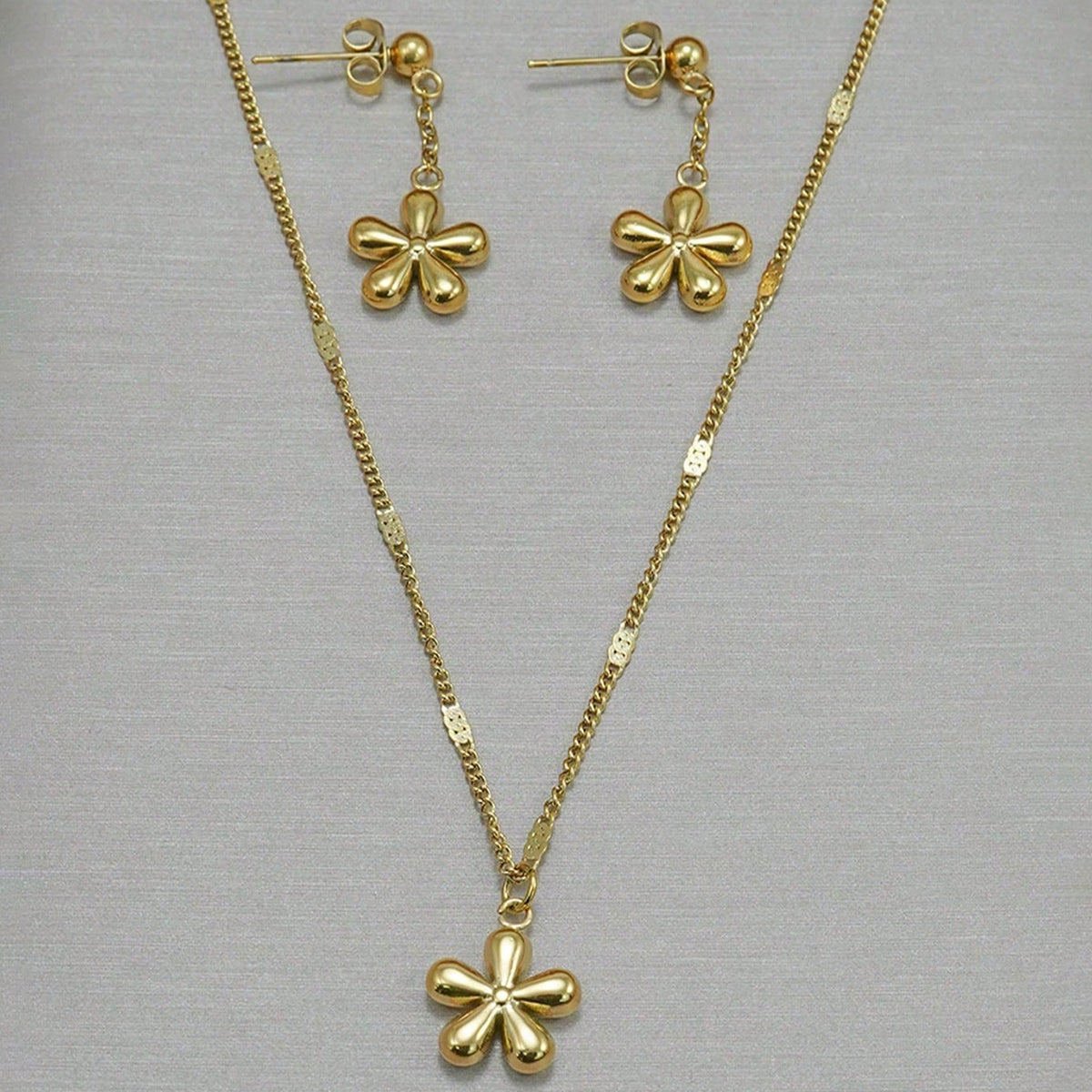 Gold necklace and earrings with clover pendants on a gray background