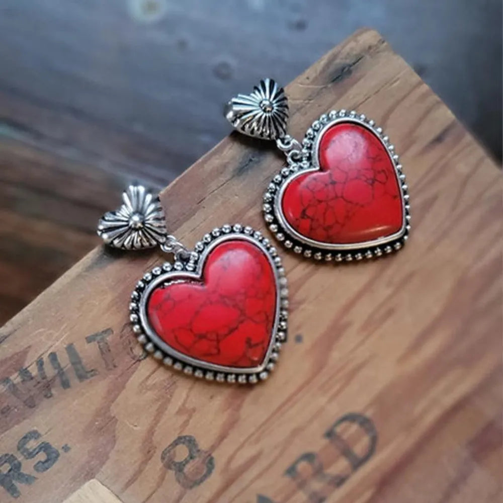 Red heart-shaped earrings with silver accents on a wooden surface