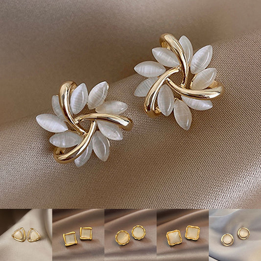 Gold and white leaf-shaped earrings on a beige fabric background