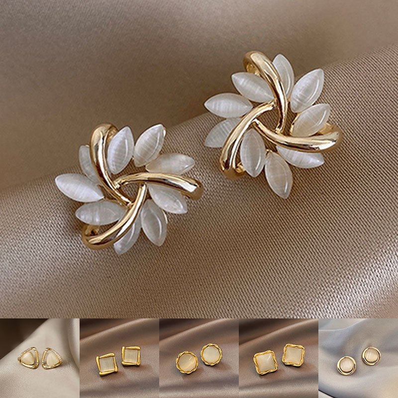 Gold and white leaf-shaped earrings on a beige fabric background
