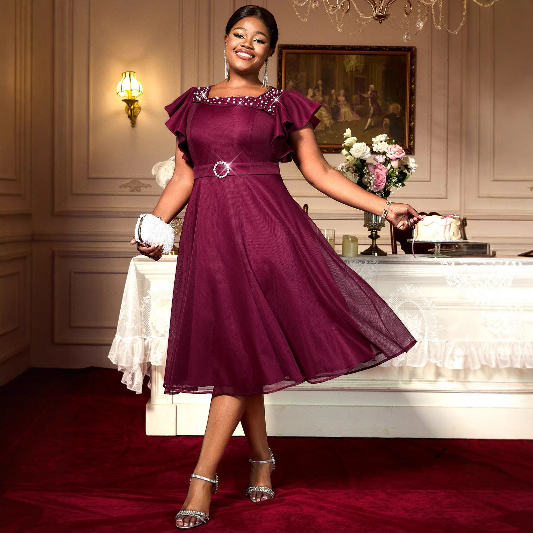 Woman in a burgundy dress standing in an elegant room with a chandelier and floral arrangement.