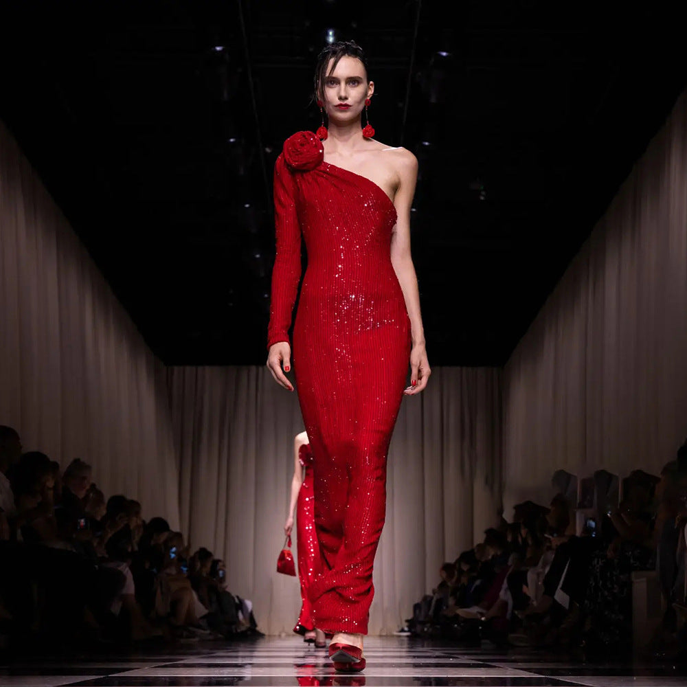 Model wearing a red one-shoulder dress on a fashion runway.