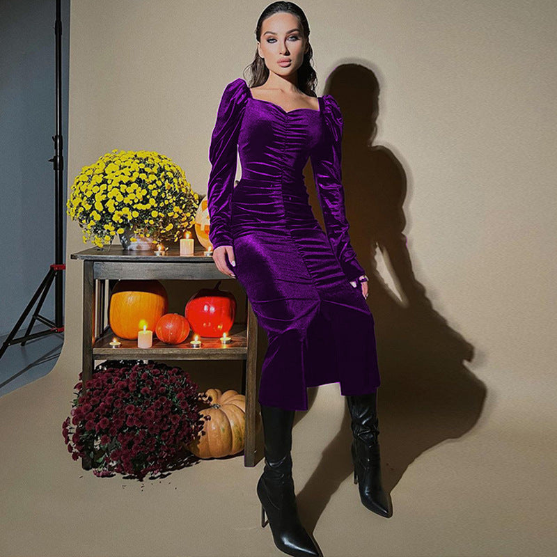 Woman in a purple dress standing in front of a decorative shelf with pumpkins and flowers.