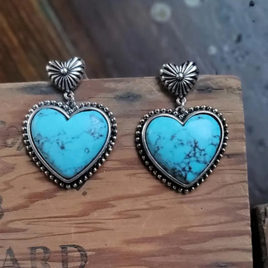 Heart-shaped turquoise earrings with silver accents on a wooden surface